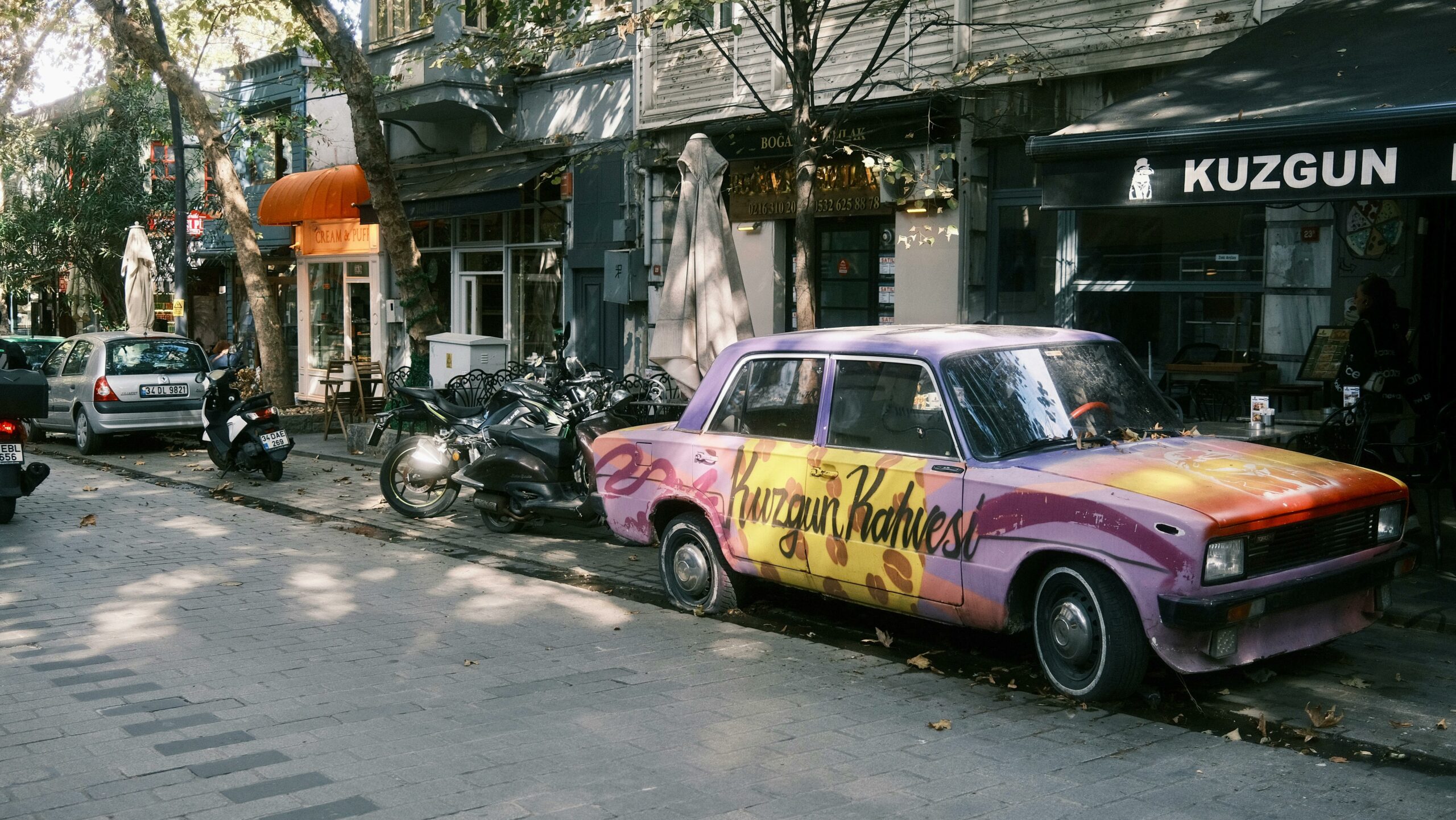 Farbenfroher Oldtimer, der in Kuzguncuk, Istanbul, geparkt ist und an einem sonnigen Tag die lokale Café-Kultur präsentiert.